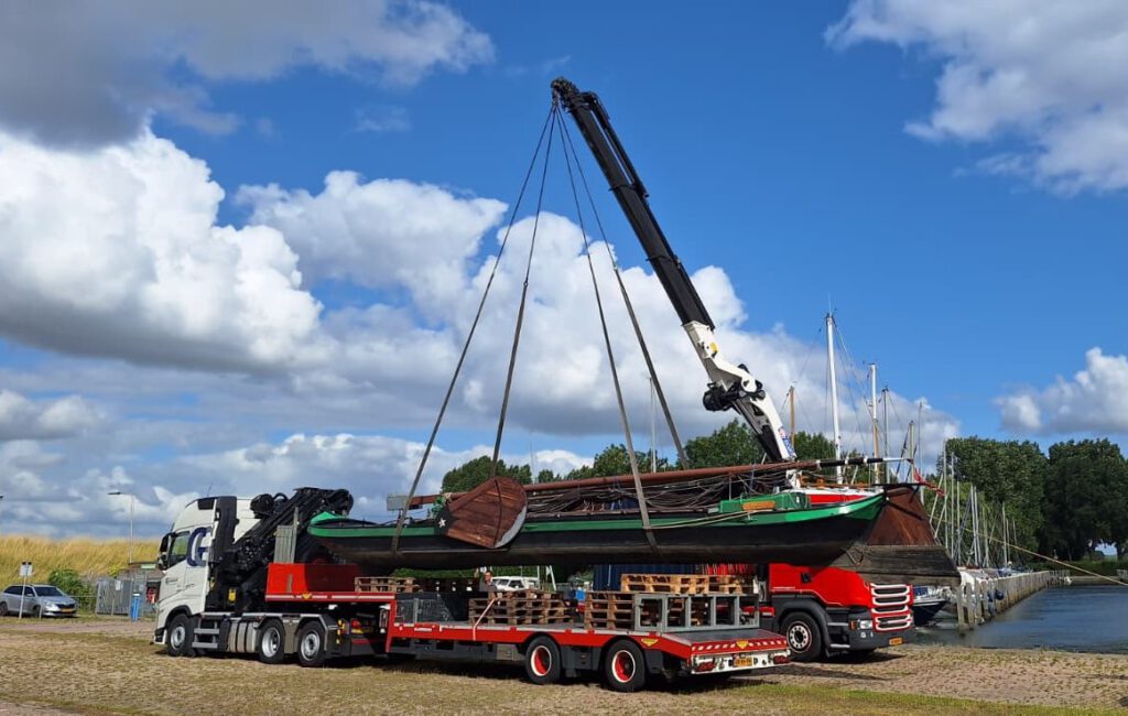Autolaadkraan hijst boot van vrachtwagen.