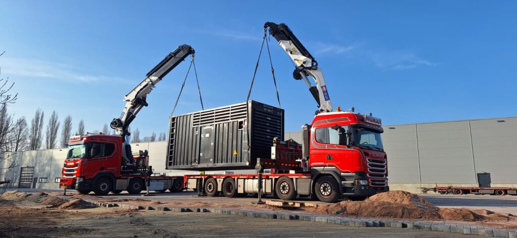 Tandem lift van container met twee rode Numan autolaadkranen.