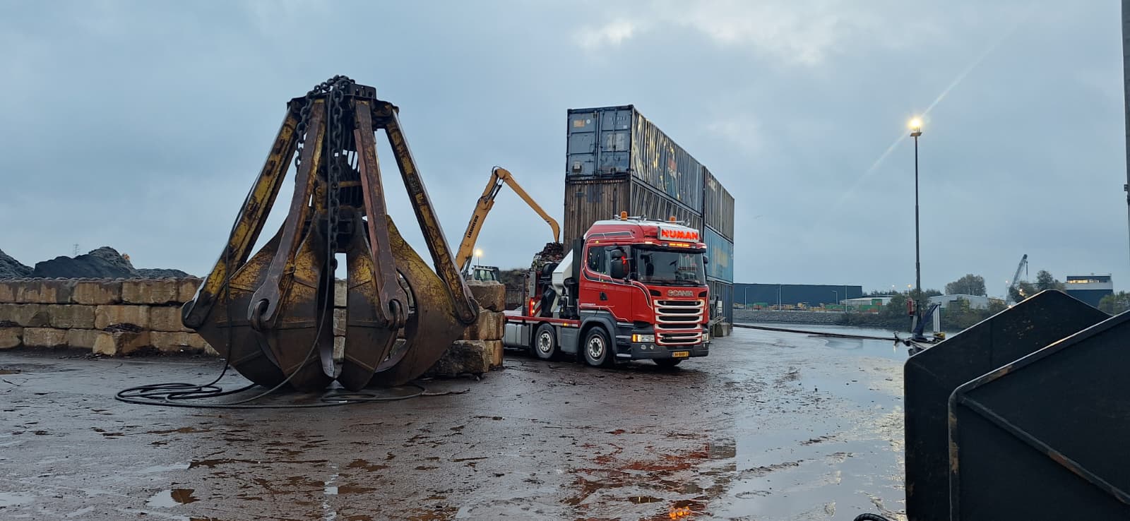 Numan Transport autolaadkraan rijdt langs containers en grote knijper.